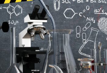 Ein Mikroskop vor einer Tafel mit chemischen Formeln, Fußabdrücken und einer Umrisszeichnung einer Person.