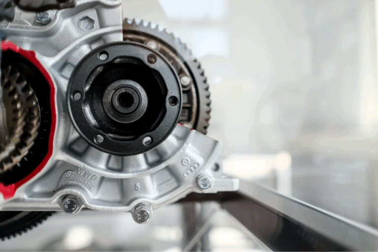 Nahaufnahme eines Metallgetriebes mit sichtbaren Zahnrädern und Befestigungsschrauben auf hellem Untergrund.