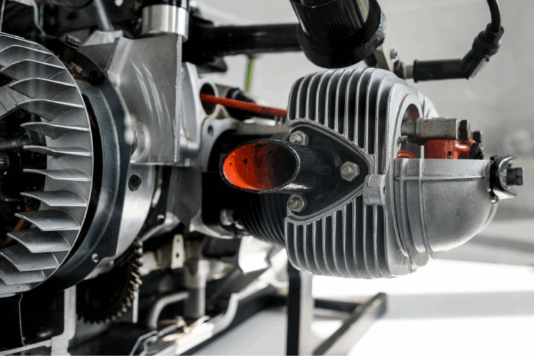 Nahaufnahme eines silbernen Motorzylinders mit Kühlrippen und orangefarbenem Innenteil an einer Maschine.