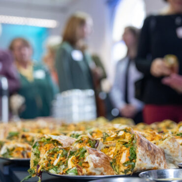 Gefüllte Wraps mit Salat und Gemüse auf einem Buffet, im Hintergrund unscharfe Personen bei einer Veranstaltung.
