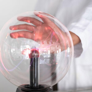 Hand berührt eine runde Plasmalampe mit sichtbaren roten und violetten Lichtbögen im Inneren.