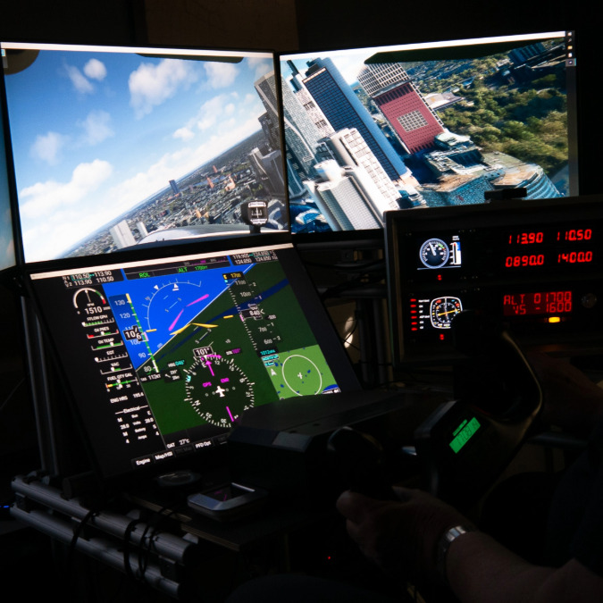 Der Flugsimulator mit drei Monitoren, die eine Stadtansicht und Fluginstrumente zeigen